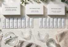 A flat-lay of at-home teeth whitening products, including strips and trays, on a bathroom counter.