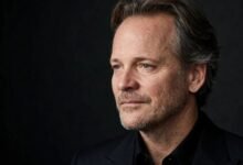 Portrait of actor Peter Sarsgaard in a dark suit against a dark studio backdrop.
