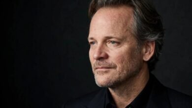 Portrait of actor Peter Sarsgaard in a dark suit against a dark studio backdrop.